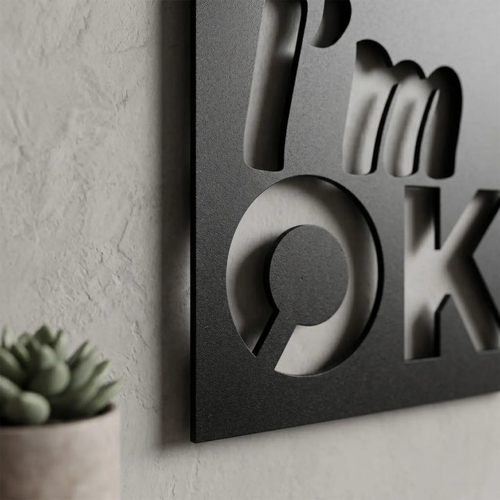 Detailopname van de metalen 'I'm OK' wanddecoratie. De matzwarte letters en afstandhouders creëren een prachtig zwevend 3D-schaduweffect aan de muur.