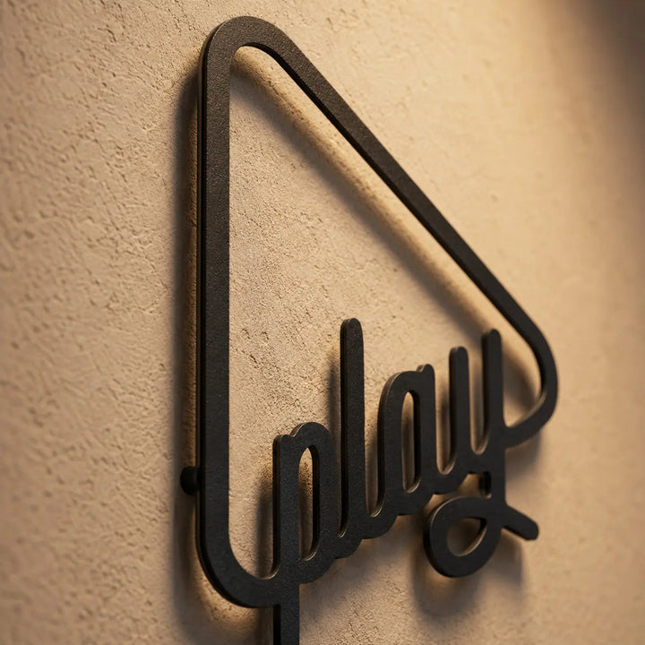 Detailopname van de metalen 'Just Play' wanddecoratie met play-knop. De afstandhouders zorgen voor een prachtig zwevend 3D-schaduweffect op de muur.