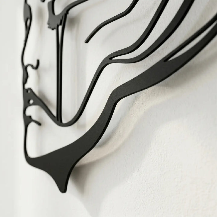 Detailopname van een zwarte metalen wanddecoratie (abstract gezicht) aan een lichte muur, die het 3D-effect en het dynamische schaduwspel door de afstandhouders benadrukt.