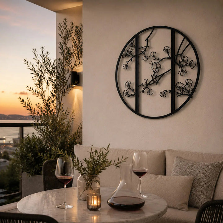 Zwarte ronde metalen wanddecoratie met bloesemtakken, sfeervol aan de muur van een overdekt balkon.
