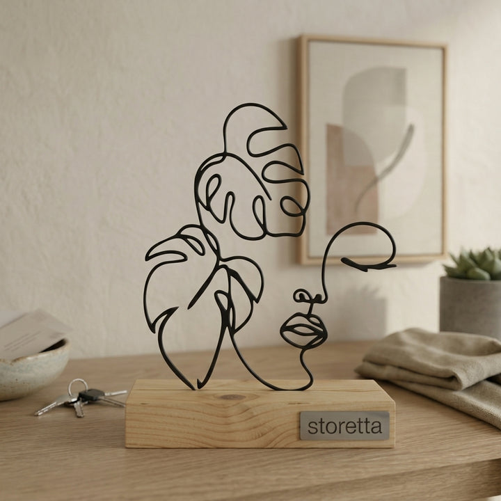 Minimalistisch decoratiebeeld van een vrouwelijk gezicht met tropische bladeren, passend bij interieurs met mangohout en staal.